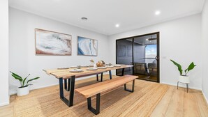 A modern dining area with a wooden table set for six, a bench, and two potted plants. - Breach House Rhyll with spa, sauna, plunge pool, EV charger (Rhyll)