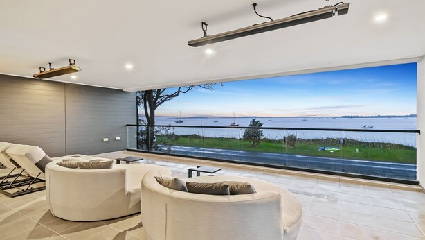 A modern living room with a large window overlooking a body of water and boats. - Breach House Rhyll with spa, sauna, plunge pool, EV charger (Rhyll)