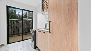 A modern kitchen with wooden cabinets, a built-in dishwasher, and a sliding glass door leading to an outdoor area. - Breach House Rhyll with spa, sauna, plunge pool, EV charger (Rhyll)