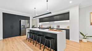 A modern kitchen with a central island, black bar stools, a built-in refrigerator, and a large window. - Breach House Rhyll with spa, sauna, plunge pool, EV charger (Rhyll)