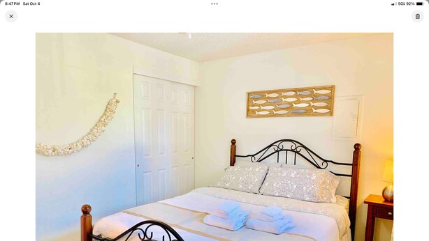 Un lit bien fait, avec une tête de lit, une table de chevet avec une lampe, et une porte visible au fond.
