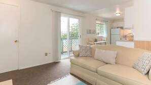 A living room with a beige sofa, patterned cushions, a small rug, and a sliding glass door leading to a balcony. - Cozy Charming and Central 1-bedroom apartment in Kent (Kent)