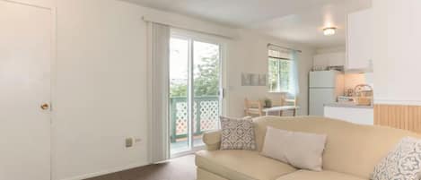 A living room with a beige sofa, patterned cushions, a small rug, and a sliding glass door leading to a balcony.