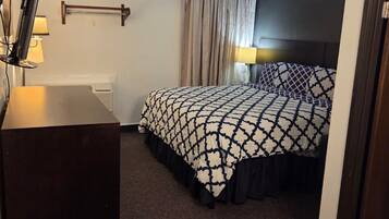A hotel room with a bed, bedside table, lamp, and a window with curtains.