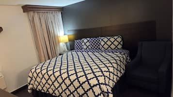 A hotel room with a bed, a chair, a nightstand, a lamp, and a window with curtains.