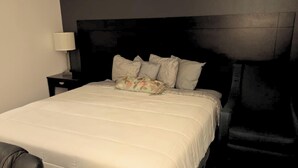 A neatly made bed with a white duvet and multiple pillows, a bedside lamp, and a dark headboard. - Blue Way Inn By Jasper Hutchinson - Standard 1 King Bed Non Smoking (Hutchinson)