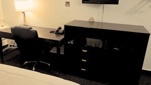 A hotel room with a bed, a desk, a chair, a TV, and a lamp. - Blue Way Inn By Jasper Hutchinson - Standard 1 King Bed Non Smoking (Hutchinson)