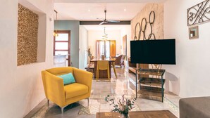A modern living room with a yellow armchair, a flat-screen TV, and a dining area with a wooden table and chairs. - Casa Kiiwik - Luxury Property with a Private Outdoor Pool and Parking in Central Merida (Mérida)