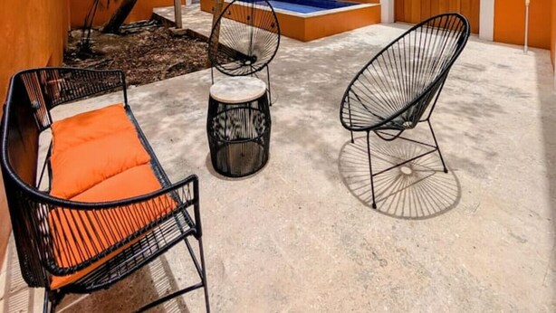 An outdoor patio with two black wireframe chairs and a small round table, a wooden door, and a tree providing shade. - Casa Axuul - Colonial Property in Central Merida (Merida)