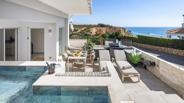 Ein moderner Außenpoolbereich mit Essplatz, Liegestühlen und Blick auf das Meer und die Klippen.