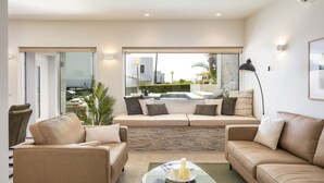 Ein modernes Wohnzimmer mit einem Glastisch, beigefarbenen Sofas und Blick auf einen Pool und eine Außenanlage.
