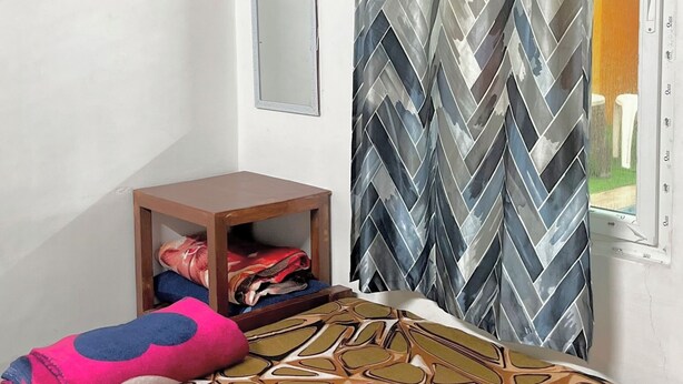 A room with a bed, a standing fan, a mirror, a wardrobe, and an air conditioning unit. - Serenity Bay Home Stay Pondicherry (Pondicherry)