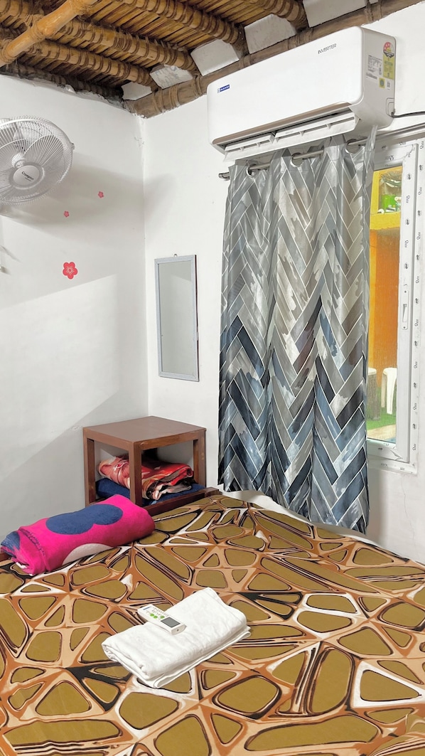 A room with a bed, a standing fan, a mirror, a wardrobe, and an air conditioning unit.