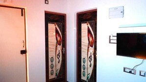 A hallway with two doors, each with a decorative design. There is a flat-screen TV mounted on the wall to the right. - Serenity Bay Home Stay Pondicherry (Pondicherry)