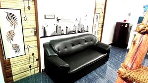A black leather sofa in a room with a cityscape wall mural, a wooden accent wall, and a blue carpet. - Serenity Bay Home Stay Pondicherry (Pondicherry)