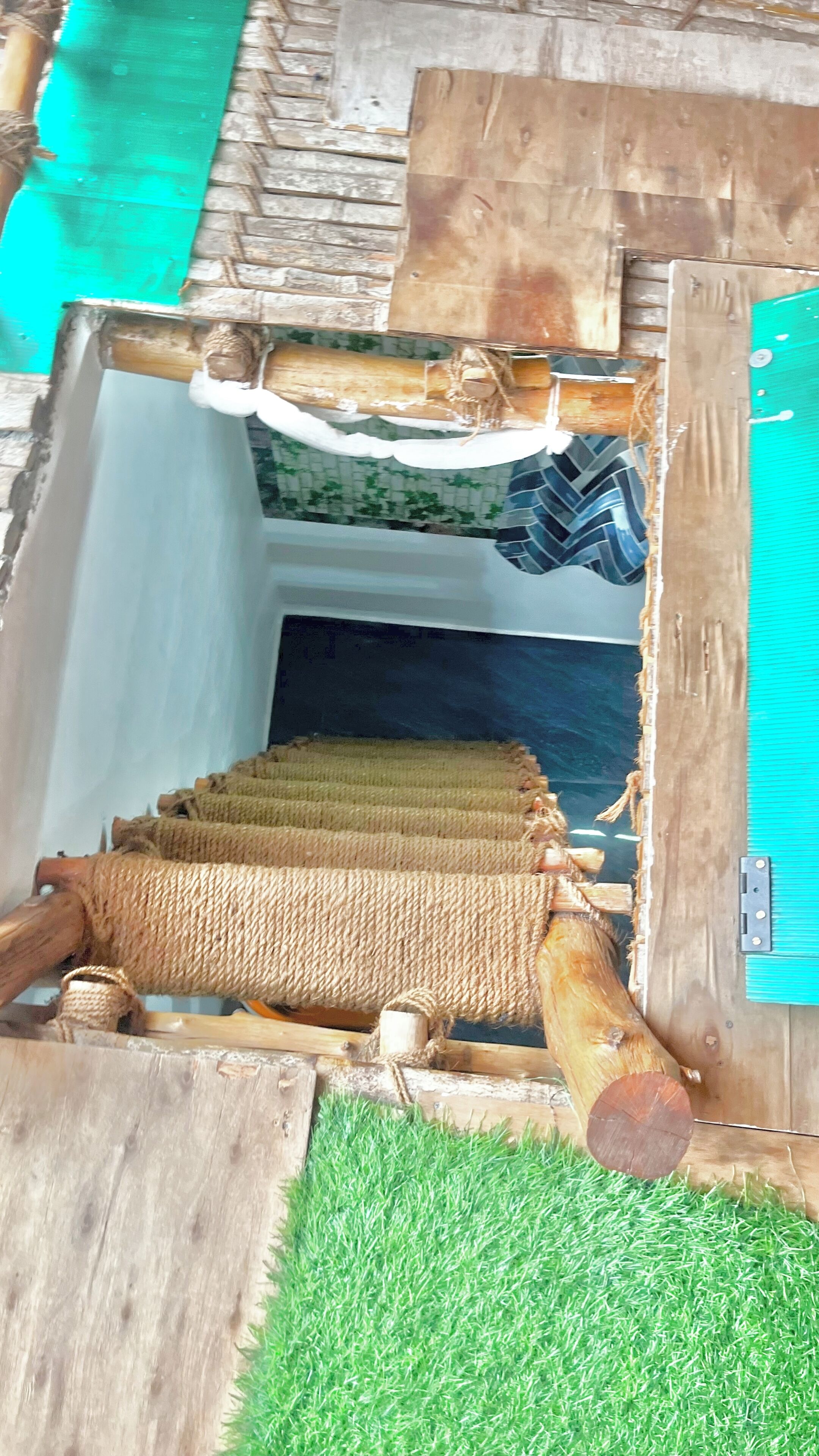 Une structure rustique en bois, avec une barrière faite de cordes, une petite entrée et une porte bleue.