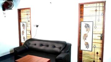 A room with a black leather sofa, a wooden coffee table, and two doors with decorative panels.