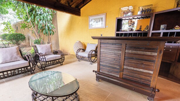 Un espace patio aménagé avec des meubles en osier, une table en verre et un chariot-bar en bois.