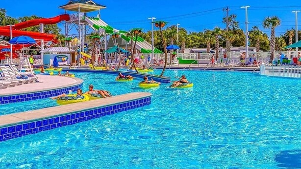 Een zwembad met meerdere banen, een waterglijbaan en loungegedeeltes met parasols.