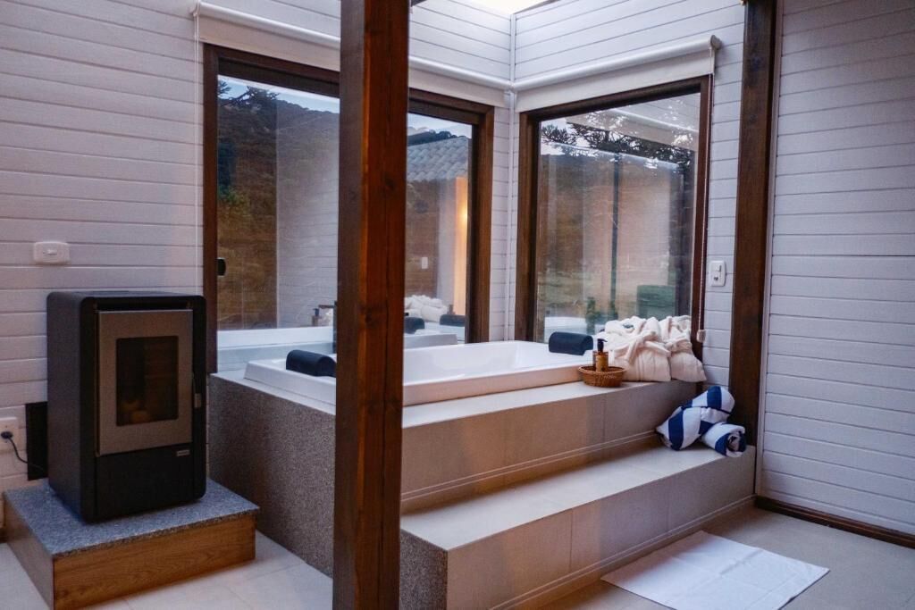 Un baño moderno con una bañera independiente, un banco de madera y una pequeña zona de estar con toallas y una cesta.