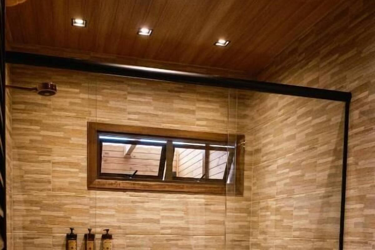 A modern bathroom with a glass-enclosed shower, a wooden ceiling, and a built-in window.