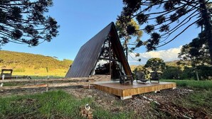 A modern building with a slanted roof, surrounded by trees and a grassy area. - Vistas de Mantiqueira (Bom Jardim da Serra)