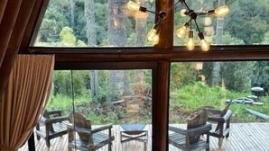 A wooden interior with large windows overlooking a deck and outdoor seating area. - Vistas de Mantiqueira (Bom Jardim da Serra)