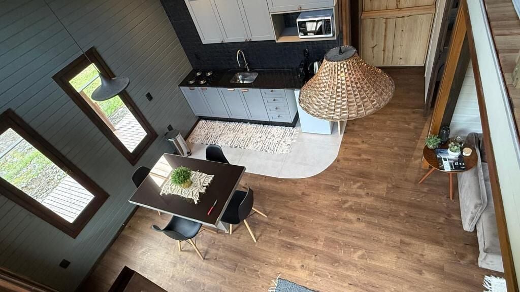 Een moderne keuken met grijze kastjes, een zwart aanrechtblad en een ingebouwde magnetron. Er is een eethoek met een tafel en stoelen, en een grote geweven lamp erboven.