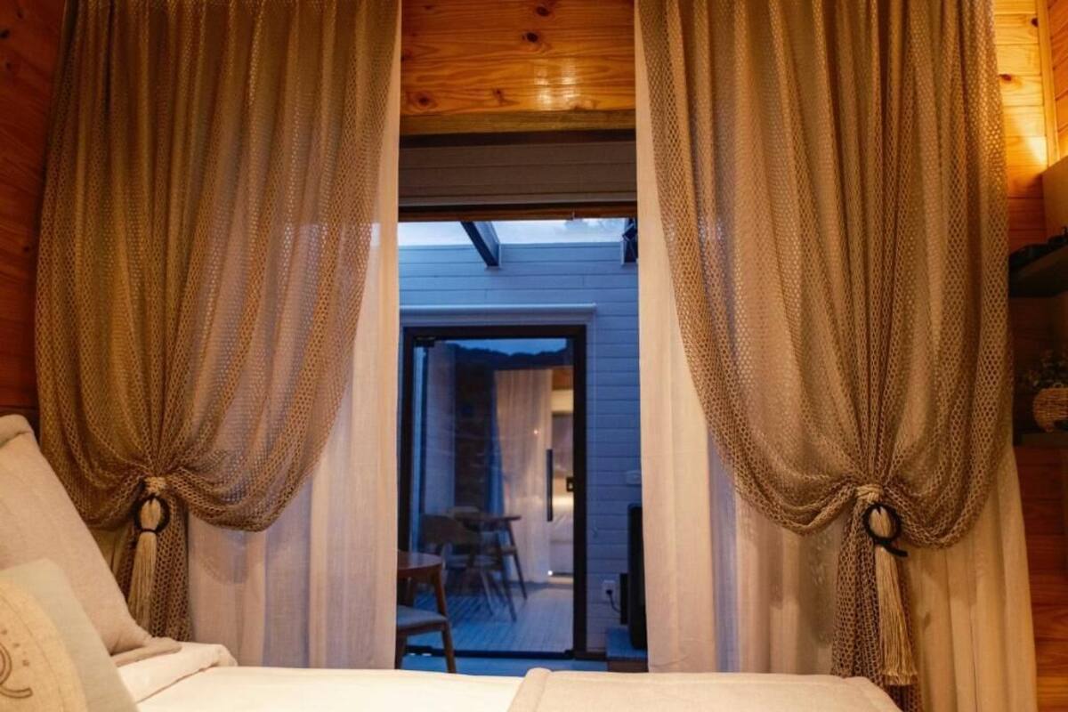 A cozy room with a bed, curtains tied back, and a view of an outdoor seating area.