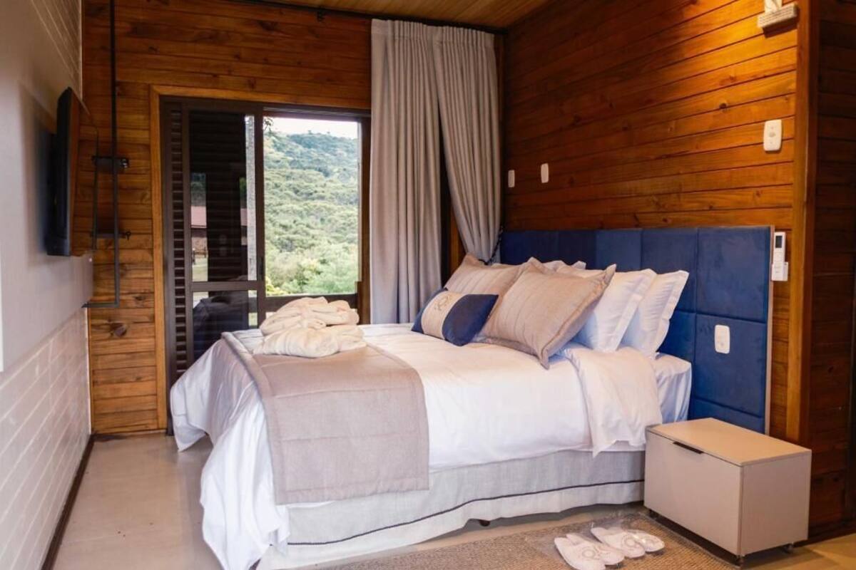 A wooden-paneled bedroom with a bed, a small bedside table, and a view of greenery outside.