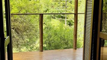 An open balcony with a wooden floor and metal railing, overlooking a lush green forest.