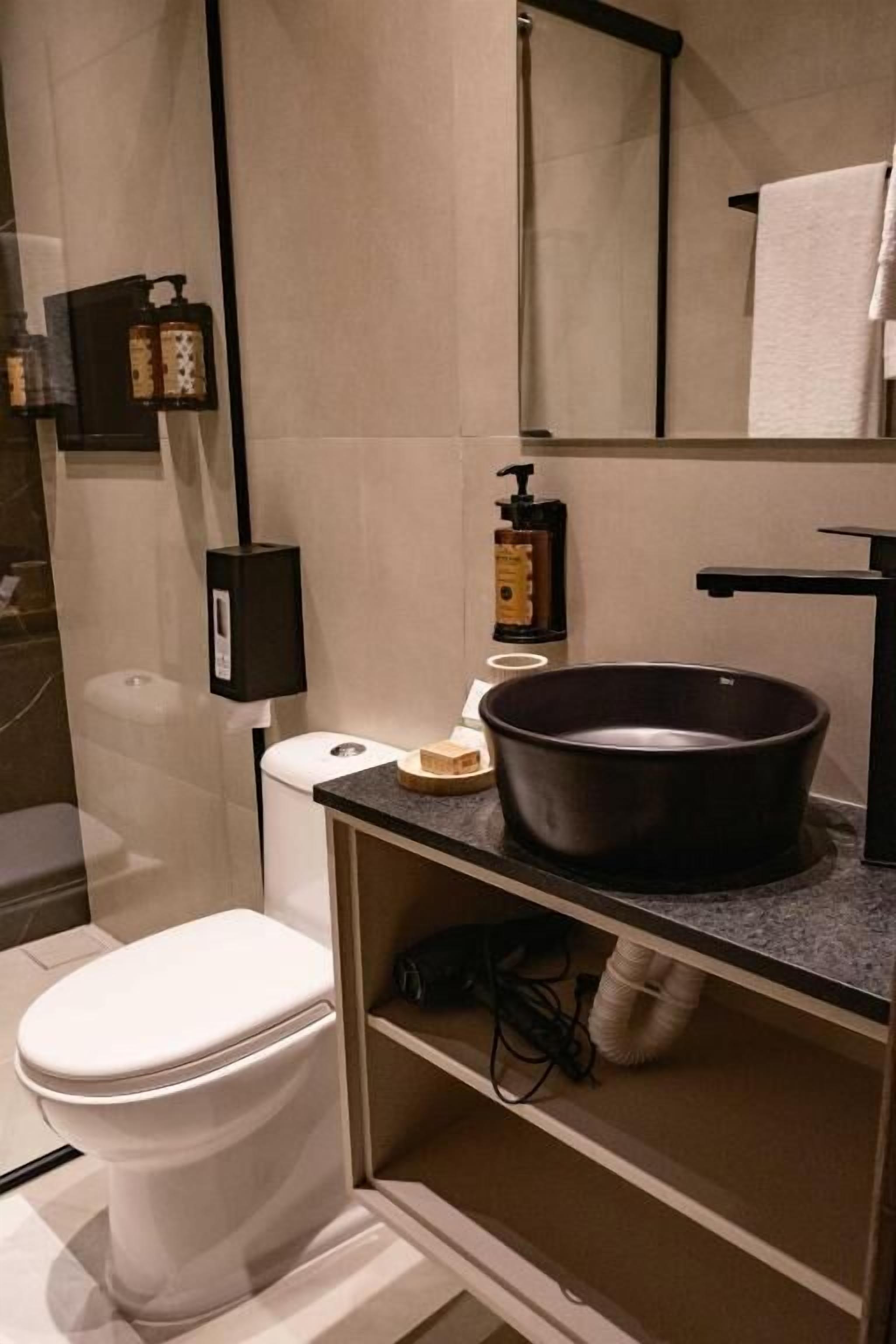 A modern bathroom with a toilet, a large mirror, a black sink, and a towel rack.