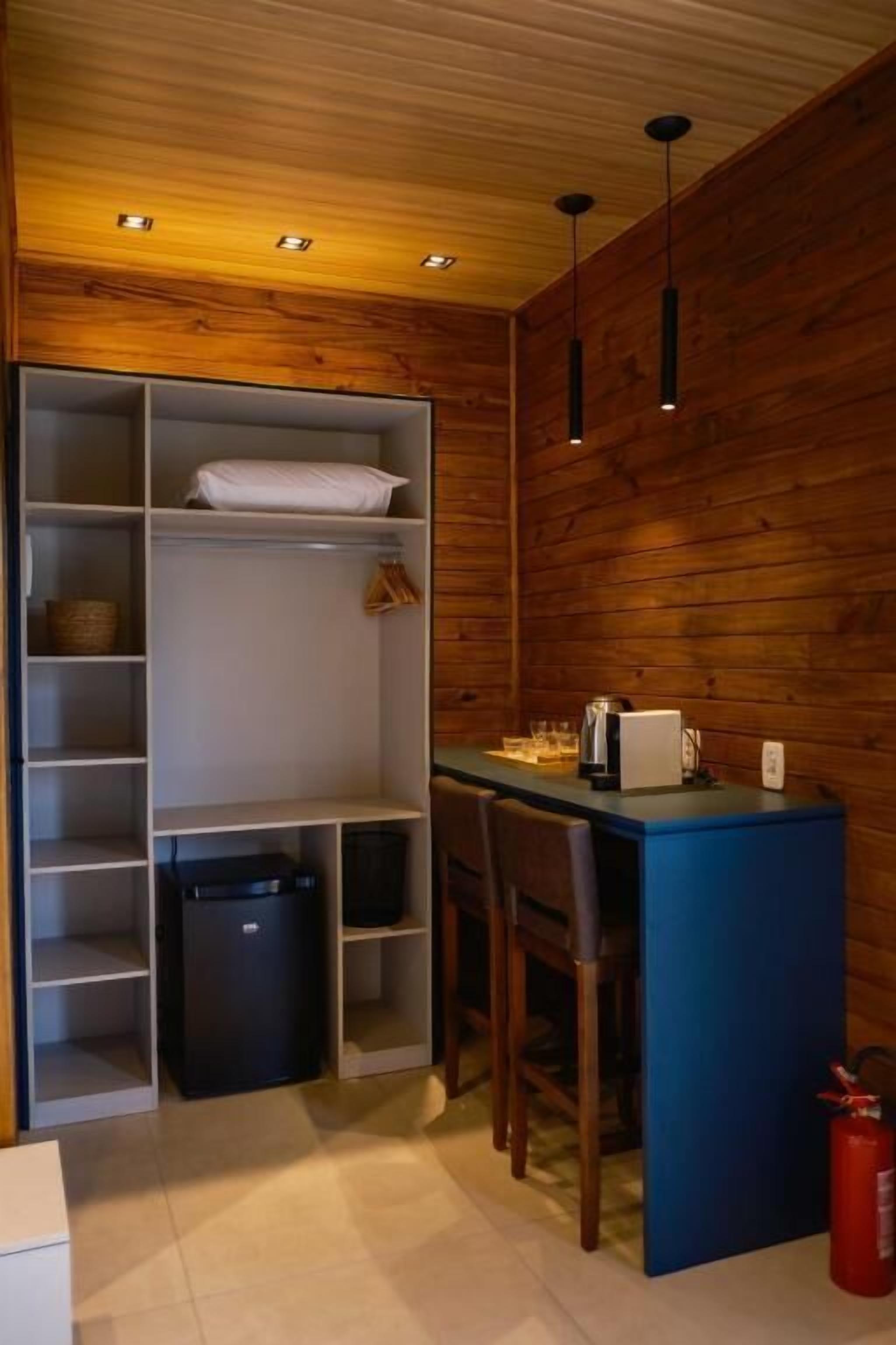 Ein kleiner Raum mit einer Holzwand, einem Tisch mit Stühlen, einer weißen Regaleinheit und einem schwarzen Mülleimer.