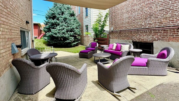 An outdoor patio with wicker furniture, a fire pit, and a brick wall. - Spacious Single Family House with Parking (Chicago)