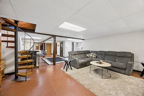 A spacious living area with a herringbone-patterned floor, a grey sectional sofa, a round coffee table, and a spiral staircase.