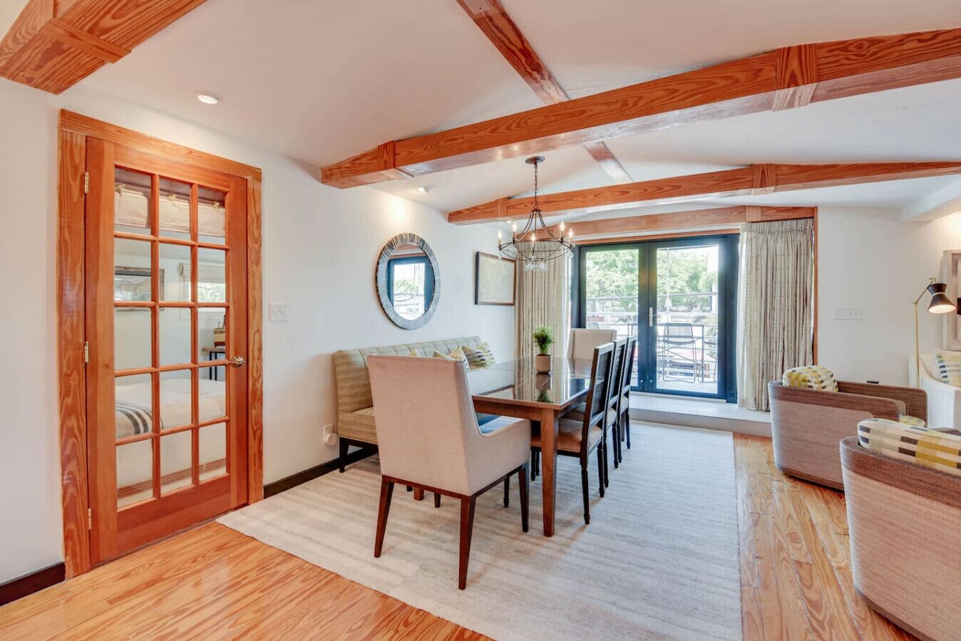 A spacious living area with a wooden ceiling, a dining table with chairs, a sofa, and a large window with curtains.
