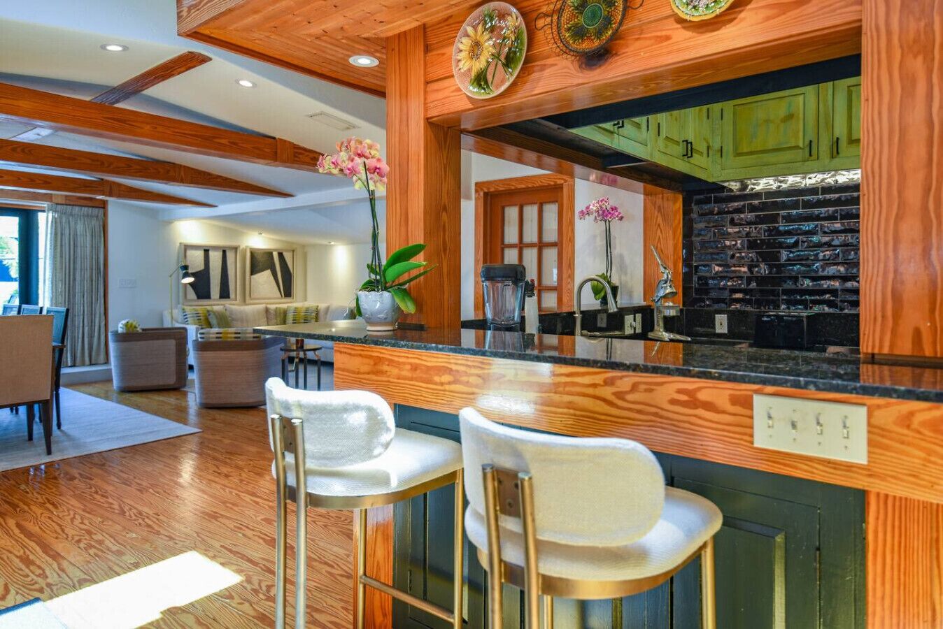 A modern kitchen with wooden accents, a black backsplash, and a bar area with two white barstools.