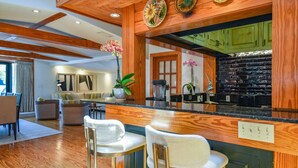 A modern kitchen with wooden accents, a black backsplash, and a bar area with two white barstools. - Slack Tide On Duval Street (Key West)