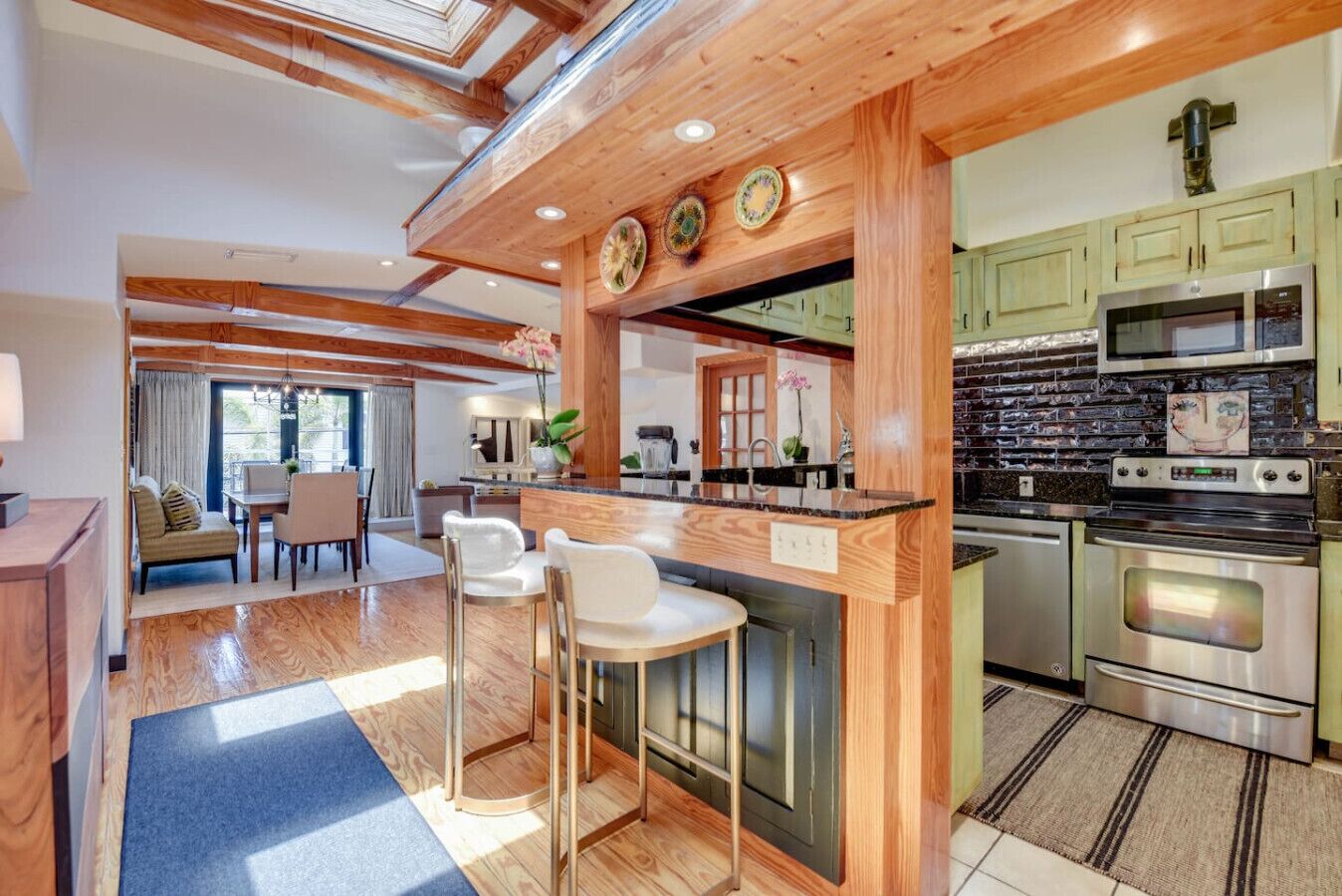 A modern kitchen with wooden beams, a central island with bar stools, and stainless steel appliances.