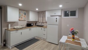 Une cuisine moderne avec des meubles blancs, un réfrigérateur, un four à micro-ondes et une table à manger agrémentée d’un vase de fleurs.