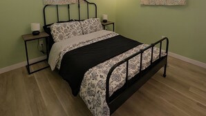 Une chambre à coucher avec un lit, deux tables de chevet, un ventilateur de plafond et une fenêtre ornée de rideaux à motifs.