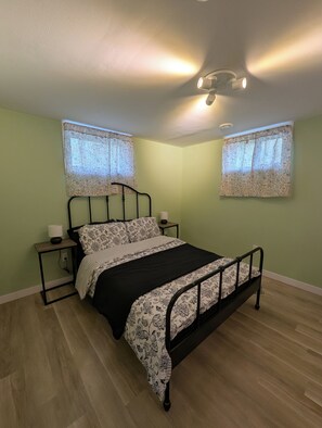 Un dormitorio con una cama, dos mesitas de noche, un ventilador de techo y una ventana con cortinas estampadas.