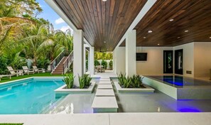 Un espace piscine moderne avec un plafond en bois, une eau cristalline et une vue sur l’extérieur.