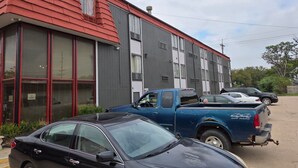 Un edificio de techo rojo y paredes grises, con coches aparcados y un cielo despejado.