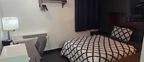 Habitación de hotel con cama, escritorio, silla, lámpara, calefactor y cortina.