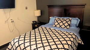 Una habitación de hotel con una cama, una mesita de noche, una lámpara y un televisor montado en la pared.