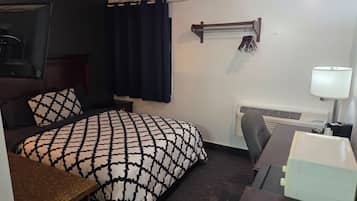A hotel room with a bed, a desk, a chair, a lamp, a heater, and a window with curtains.