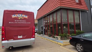Un autobús rojo Beeline Express estacionado frente a un edificio con ventanas amplias y techo rojo.