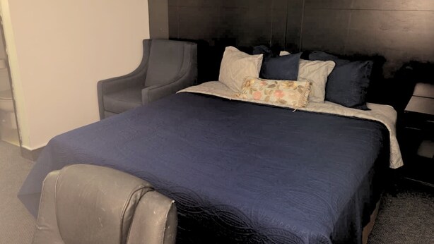 Ett hotellrum med ett mörkblått sängöverkast, en grå fåtölj och en sänggavel.
