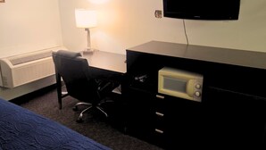 Ett hotellrum med en säng, ett skrivbord med en dator, en lampa, en tv och en mikrovågsugn.